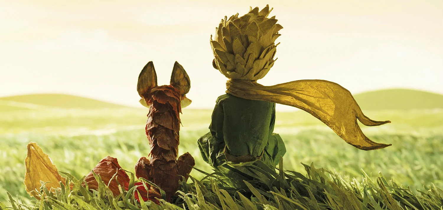 Szenenbild: Der Fuchs und der kleine Prinz sitzen auf einer Wiese